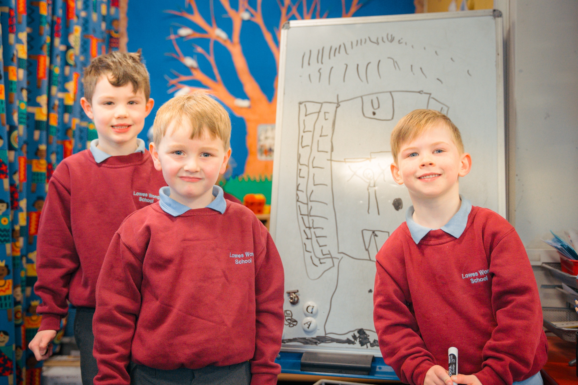 three students smiling to camera in front of white board